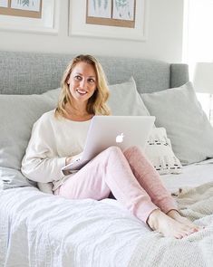 a woman is sitting on her bed with a laptop in her lap and smiling at the camera