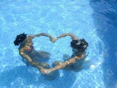 two people are in the water making a heart shape with their hands and holding onto each other