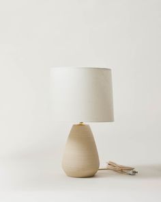 a wooden table lamp with a white shade on the base and a cord plugged into it