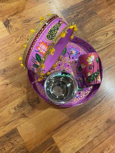 a purple purse sitting on top of a wooden floor next to a glass bowl with a silver lid