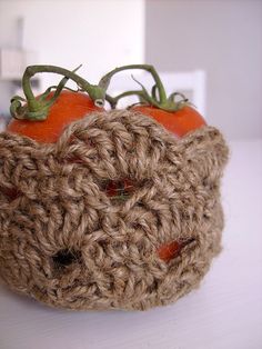 two orange tomatoes sitting in a crocheted basket on top of a white table