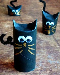 three black cat made out of toilet paper on top of a wooden table with googly eyes