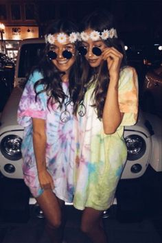 two young women standing next to each other in front of a car with flowers on their head