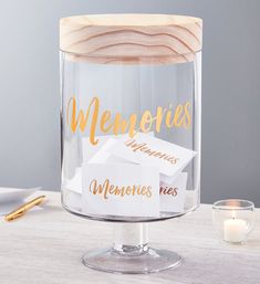 a clear glass with gold lettering on it sitting on a table next to a candle