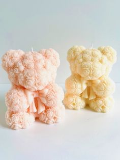 two small teddy bears sitting next to each other on a white surface with one holding a candle in its mouth