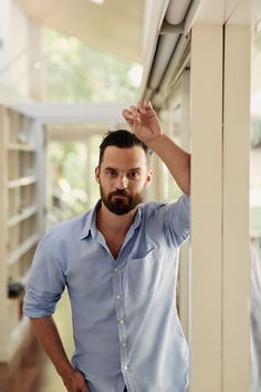 a man standing in front of a window with his hand up to the light fixture