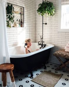 a child sitting in a bathtub next to a table and potted plants on the wall