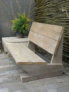 a wooden bench sitting on top of a brick floor next to a potted plant