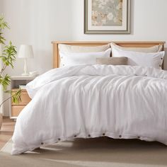 a bed with white linens and pillows in a small room next to a potted plant