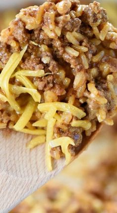 a wooden spoon filled with macaroni and cheese on top of a casserole dish