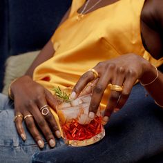 a woman sitting on a couch holding a cocktail glass filled with ice and garnishes