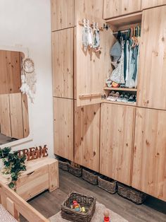 a room with wooden cabinets and clothes hanging on the wall, baskets in front of it