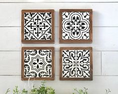 four black and white tiles mounted on a wall next to some green plants in front of it