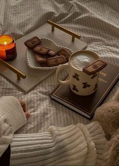 a cup of coffee and some cookies on a bed with a teddy bear next to it