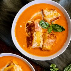 two bowls of tomato soup with grilled bread and basil garnish on top