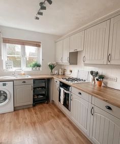 a kitchen with wooden floors and white cabinets, an oven, dishwasher and washing machine