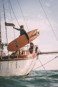 a man holding a surfboard standing on top of a boat in the ocean,