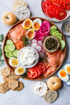 an assortment of vegetables and meats on a platter with crackers, tomatoes, cucumbers, onion rings, bread