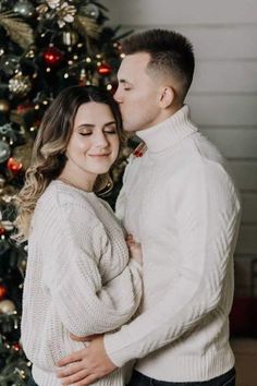 a man and woman standing in front of a christmas tree with their arms around each other