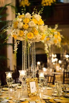 a tall vase filled with yellow and white flowers on top of a dining room table