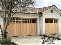 a white brick house with two brown garage doors and a tree in the front yard