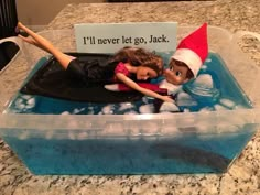 there is a plastic container with two dolls in it on the counter top, and an ice tray that says i'll never let go jack