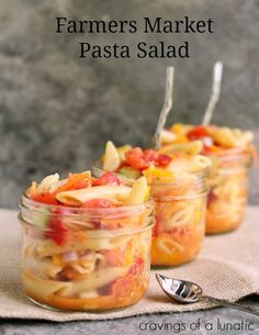 three mason jars filled with pasta salad on top of a cloth next to a spoon