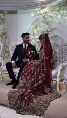 a bride and groom sitting on a bench in front of a floral backdrop at their wedding