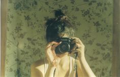 a woman holding a camera up to her face in front of a floral wallpaper