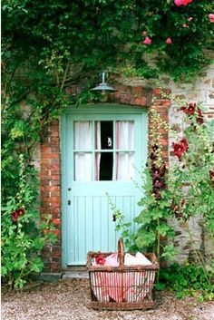 a blue door surrounded by greenery and flowers in front of a brick building with a basket on the ground