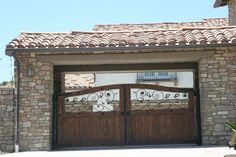 a large wooden gate with wrought iron work on the top and bottom panels, in front of a house