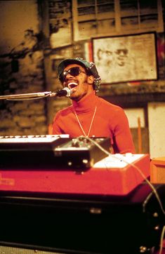 a man with sunglasses and a hat on singing into a microphone in front of a keyboard