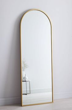 a mirror sitting on top of a floor next to a white vase with a plant in it