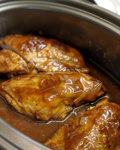 two pieces of cooked chicken are in the slow cooker with brown gravy