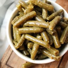 a white bowl filled with green beans on top of a wooden cutting board