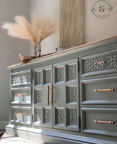 an old dresser painted gray with gold hardware and feathers on top, in a living room