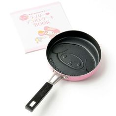 a pink and black frying pan sitting on top of a white table next to a book