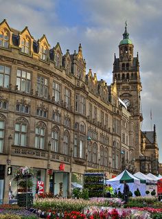 an old building with many flowers in the foreground and a clock tower in the background