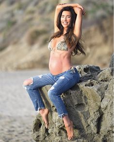 a woman sitting on top of a rock next to the ocean with her arms behind her head