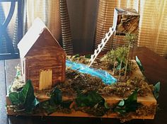 a wooden table topped with miniature houses and plants on top of wood planks next to a window