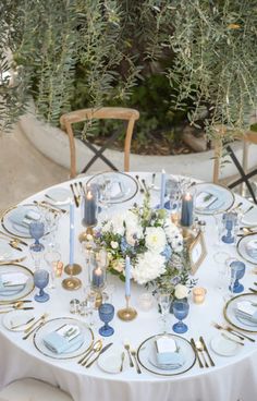 the table is set with blue and white plates, silverware, flowers and candles