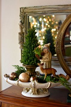 a small christmas tree is on top of a table with ornaments and a mirror in the background