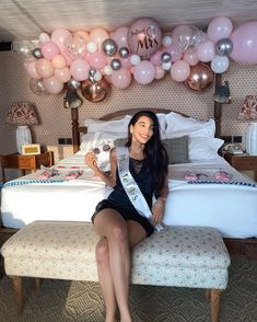 a woman sitting on top of a bed next to balloons