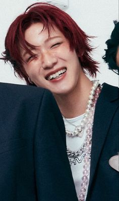 a person with red hair and a suit jacket smiling at the camera while wearing pearl necklaces