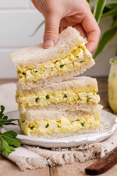 someone is holding two slices of egg salad sandwich on a white plate with parsley