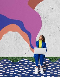 a woman sitting on a chair in front of a colorful wall