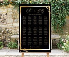 a black and gold wedding seating chart on a wooden easel in front of a stone wall