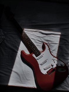 a red electric guitar sitting on top of a white sheet