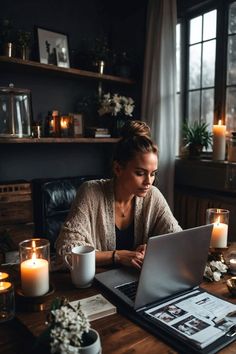 a woman sitting at a table with a laptop in front of her, surrounded by candles