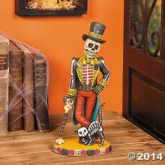 a skeleton figurine with a top hat and cane stands in front of an orange wall